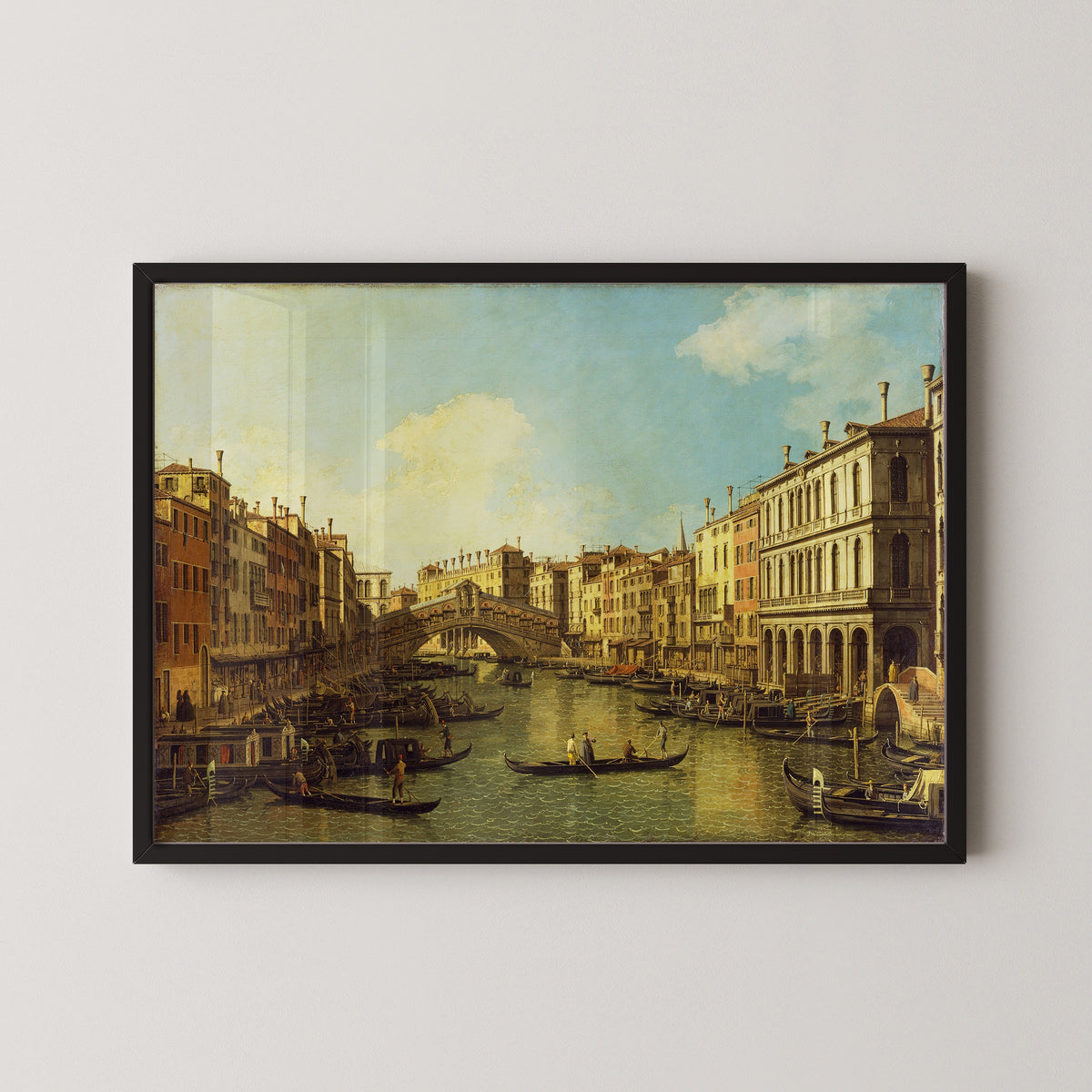 Framed art print of Venice, the Grand Canal from the Palazzo Dolfin-Manin to the Rialto Bridge by Canaletto, in a black frame on a pale wall