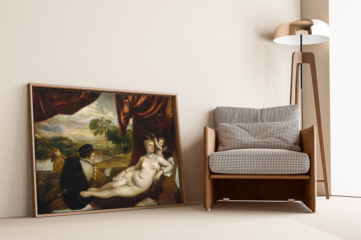 Framed art print of Venus and the Lute Player by Titian, leaning against a wall beside an armchair and a floor lamp