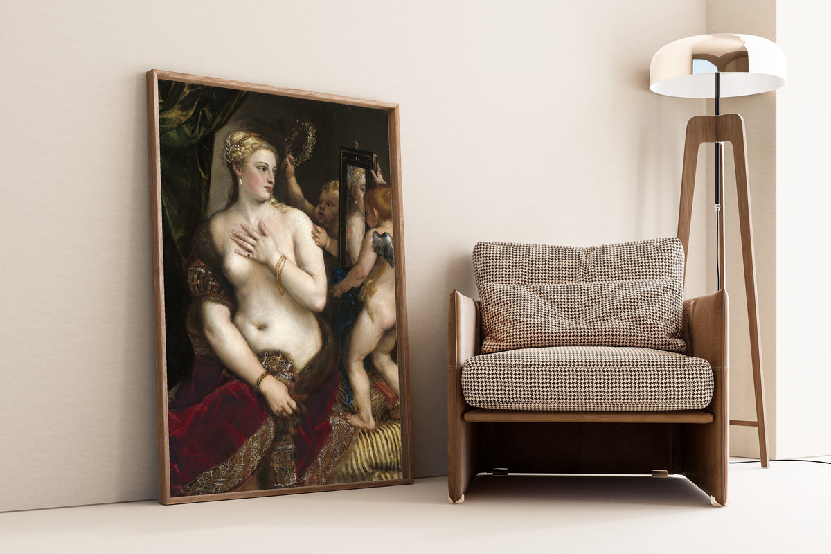 Framed art print of Venus with a Mirror by Titian, leaning against a wall beside an armchair and a floor lamp
