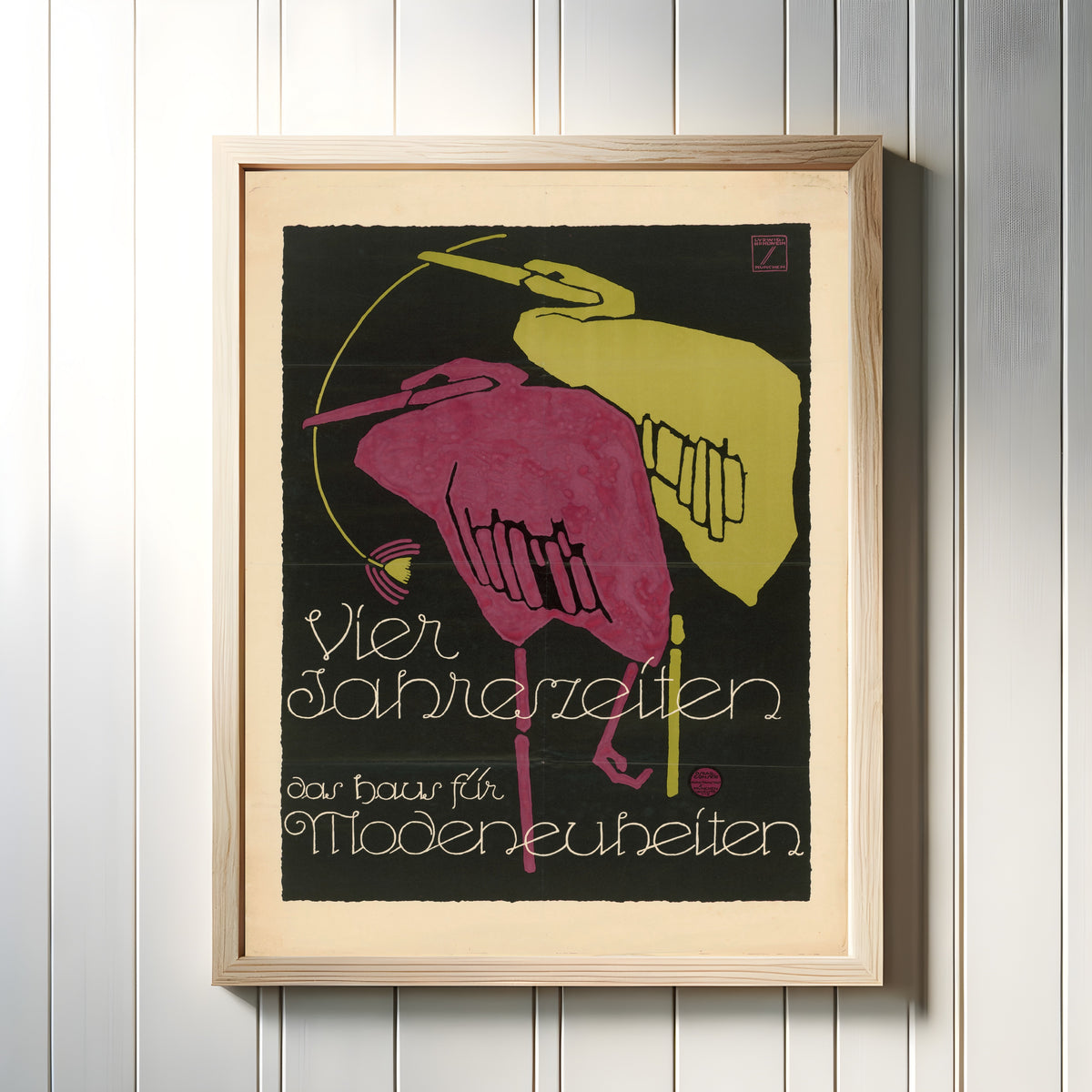 Framed art print of Vier Jahreszeiten: Das Haus für Modeneuheiten by Ludwig Hohlwein, in a light wood frame on a white panelled wall