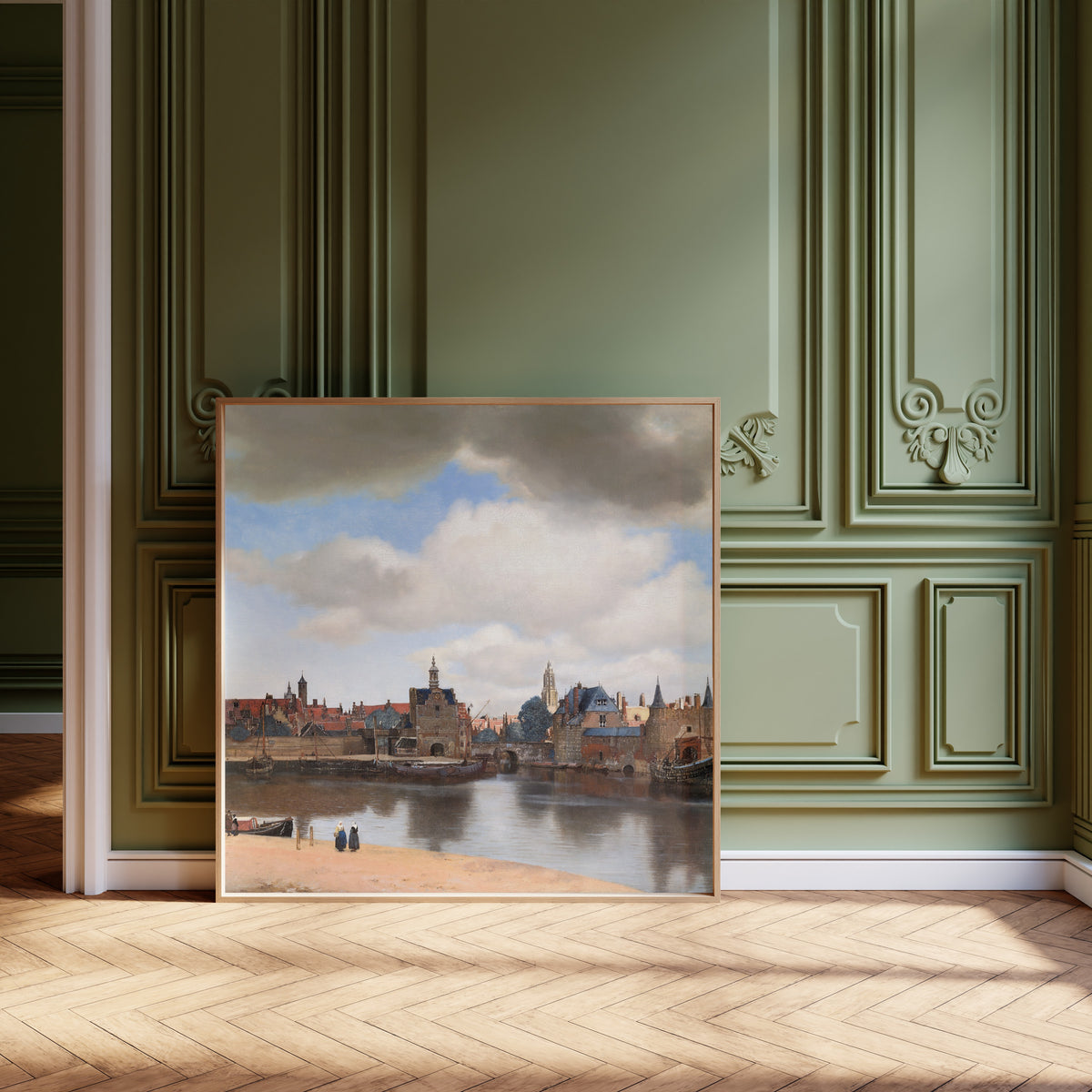 Framed art print of View of Delft by Johannes Vermeer, leaning against olive-green panelling on a herringbone floor