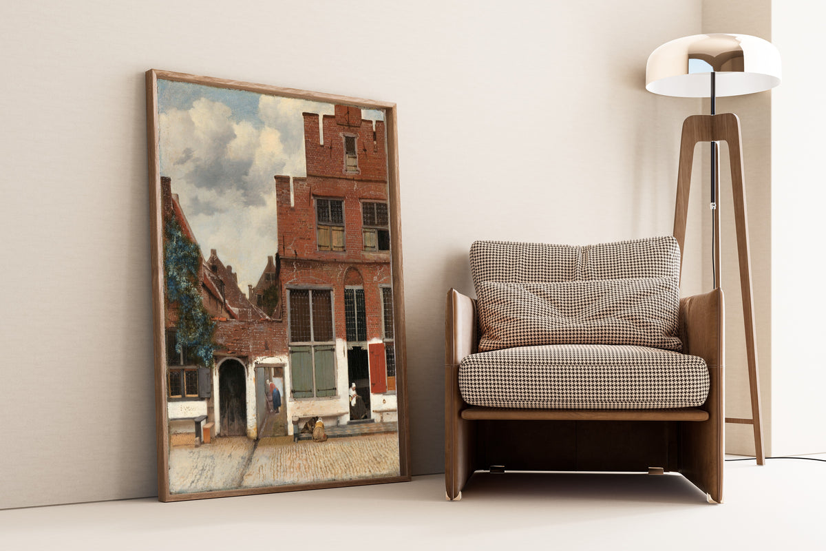 Framed art print of View of Houses in Delft, Known as ‘The Little Street’ by Johannes Vermeer, leaning against a wall beside an armchair and a floor lamp