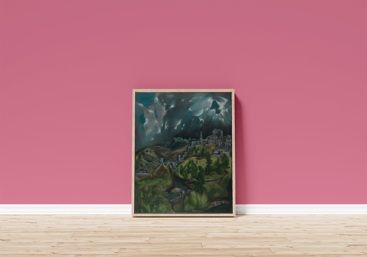 Framed art print of View of Toledo by El Greco, in a light wood frame leaning on a pink wall above a wooden floor