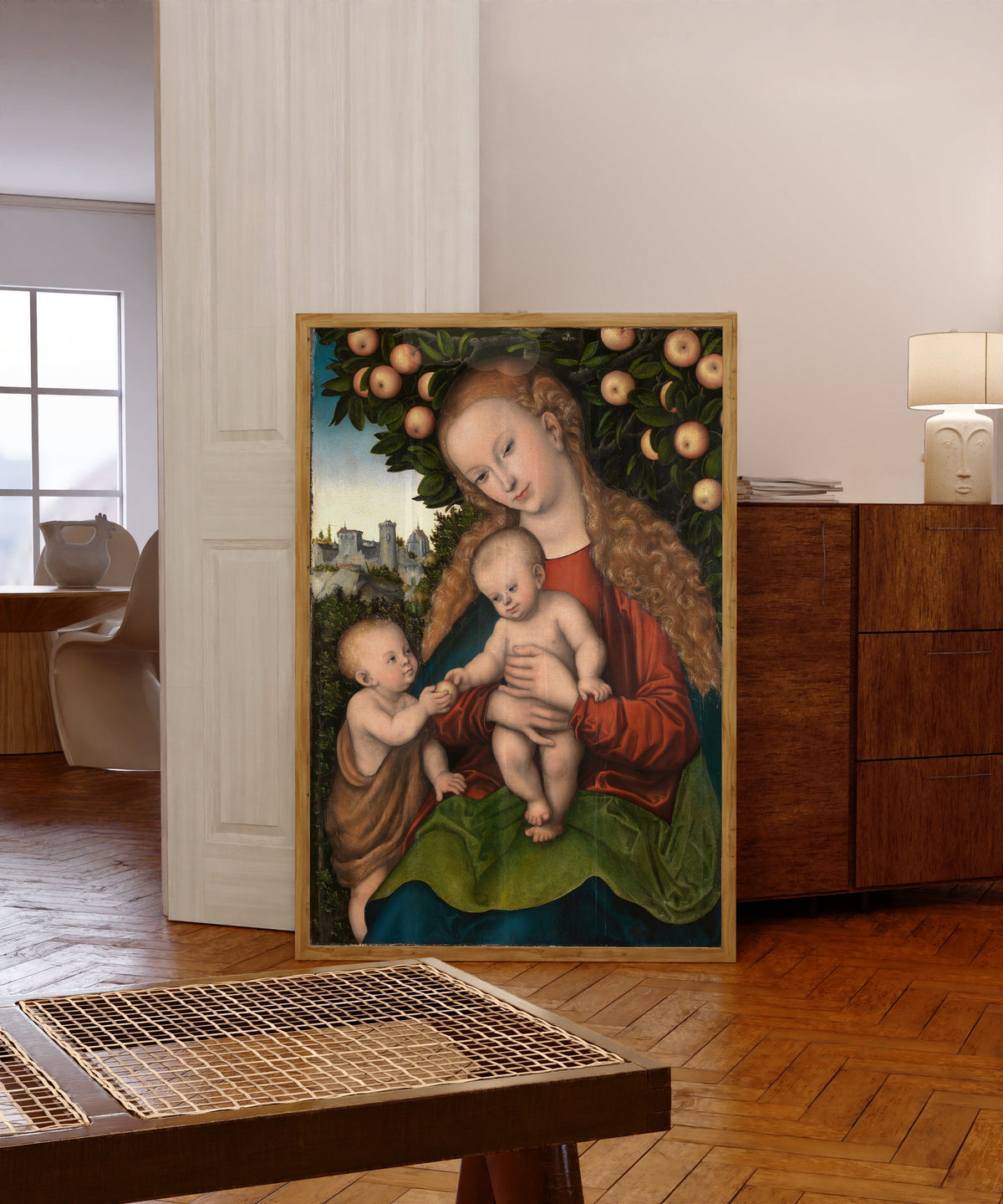 Framed art print of Virgin and Child with Saint John under an… by Lucas Cranach the Elder, in a light wood frame leaning in a warm room with a parquet floor