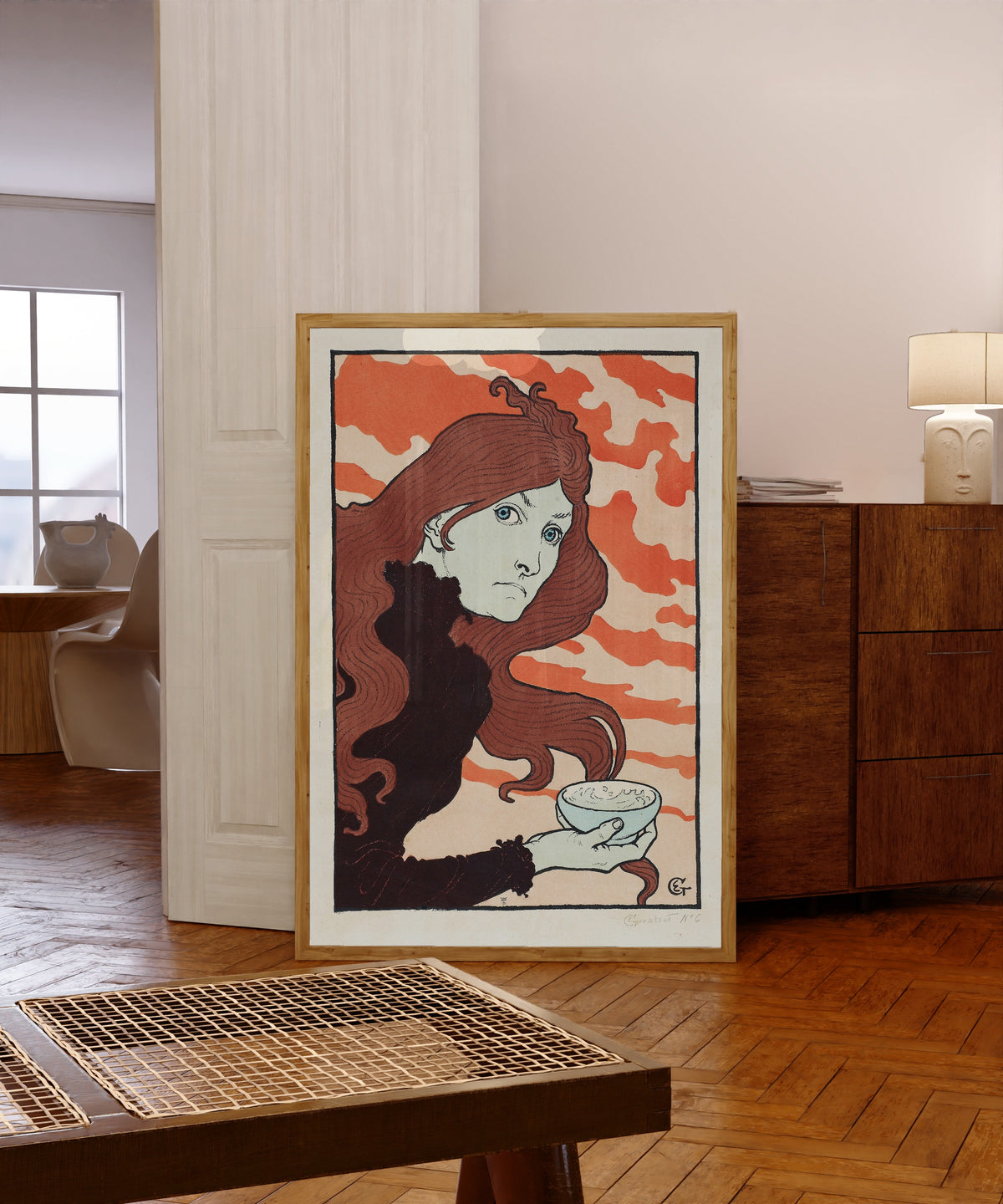 Framed art print of Vitrioleuse (The Acid Thrower) by Eugène Grasset, in a light wood frame leaning in a warm room with a parquet floor