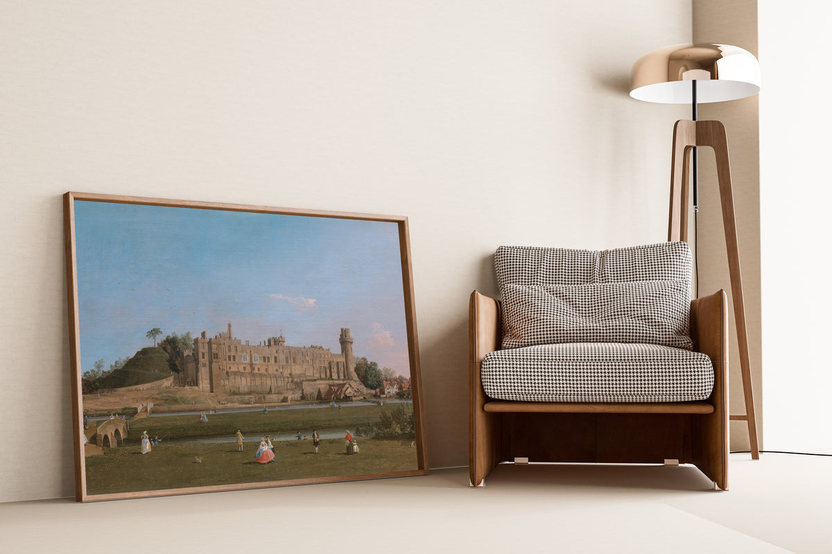 Framed art print of Warwick Castle by Canaletto, leaning against a wall beside an armchair and a floor lamp