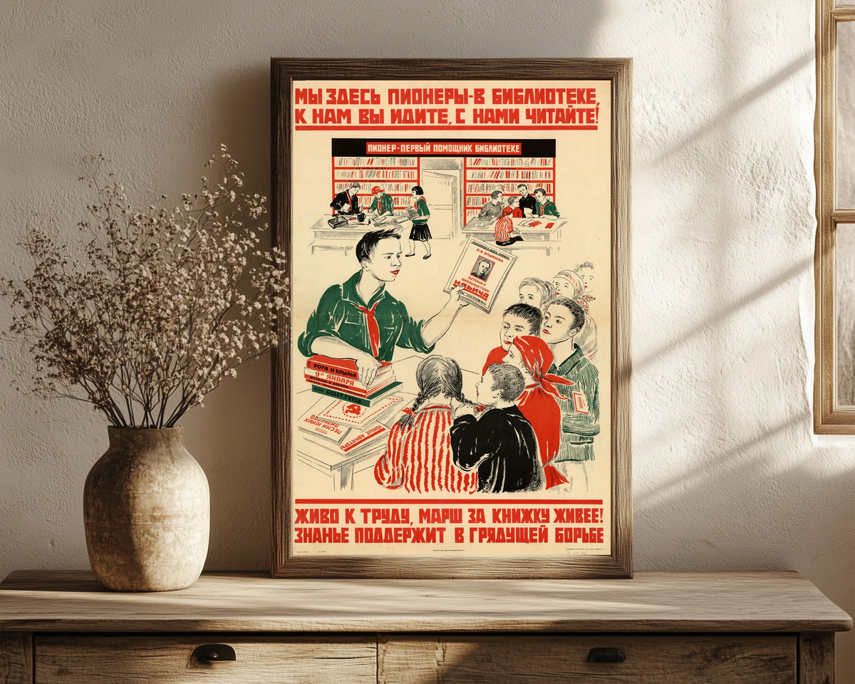 Framed art print of We pioneers are here in the library: come to us, read with us!, in a dark wood frame leaning on a rustic console beside dried flowers