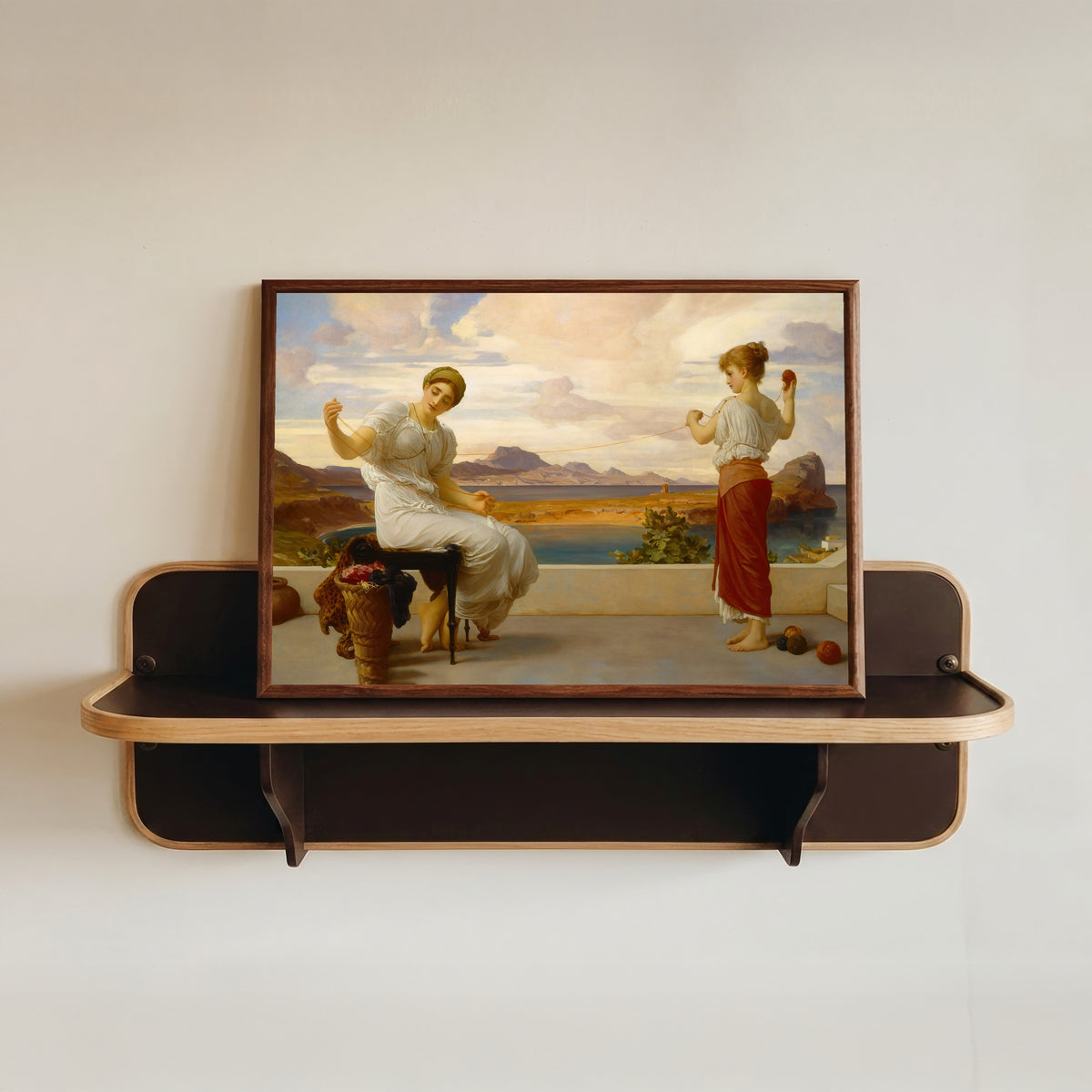 Framed art print of Winding the Skein by Frederic Leighton, in a dark wood frame resting on a wall shelf
