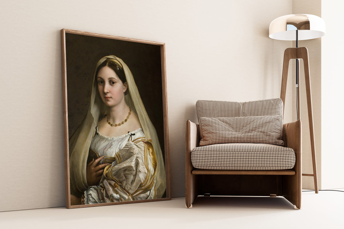 Framed art print of Woman with a Veil by Raphael, leaning against a wall beside an armchair and a floor lamp