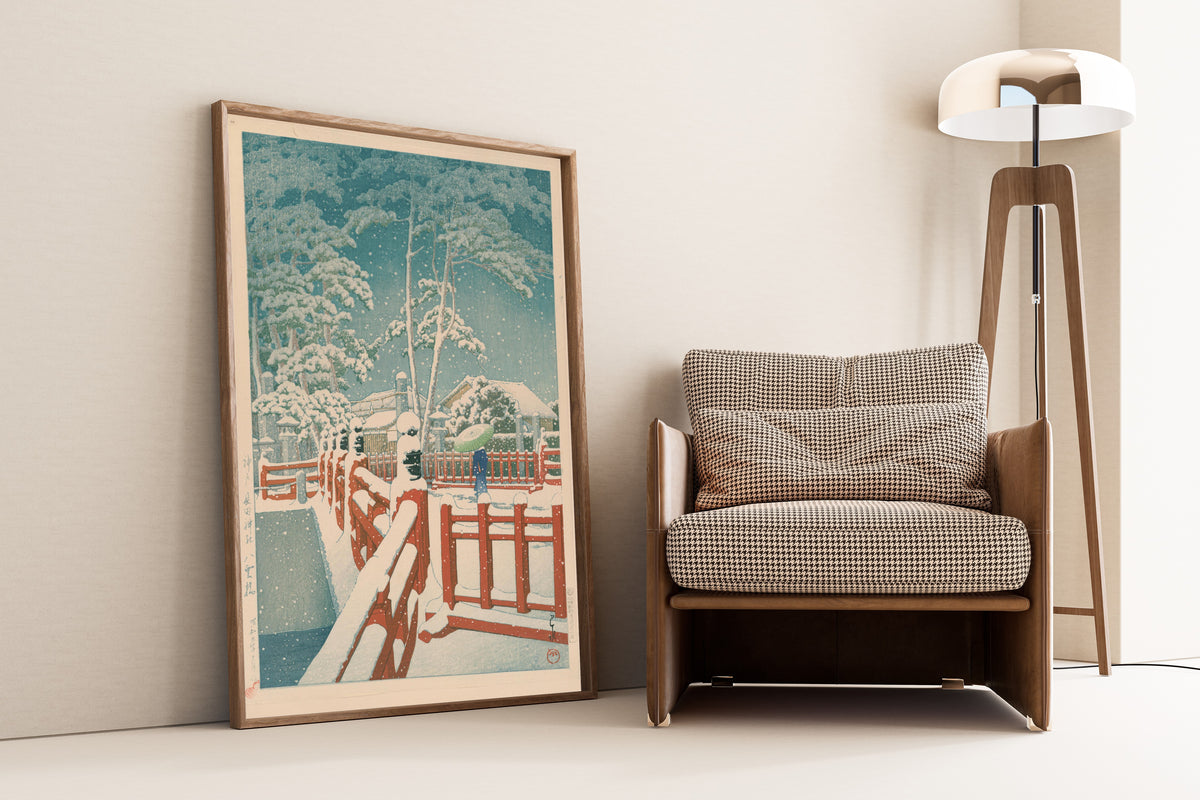 Framed art print of Yakumo Bridge at Nagata Shrine, Kobe by Kawase Hasui, leaning against a wall beside an armchair and a floor lamp