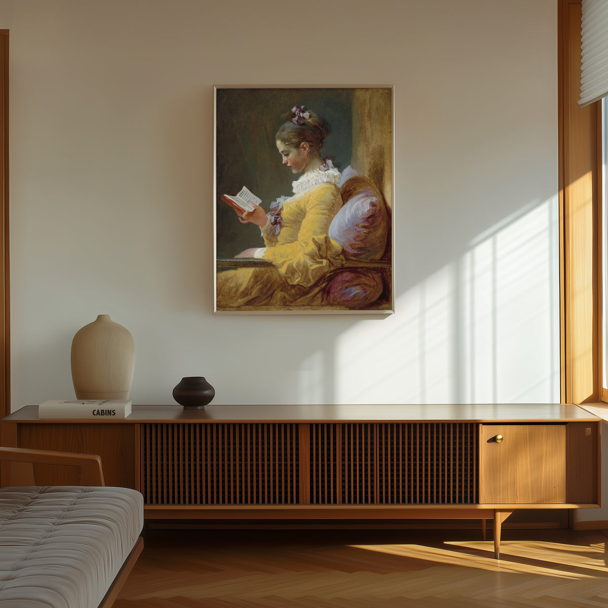 Framed art print of Young Girl Reading by Jean-Honoré Fragonard, in a thin light frame on a sunlit wall above a wooden sideboard