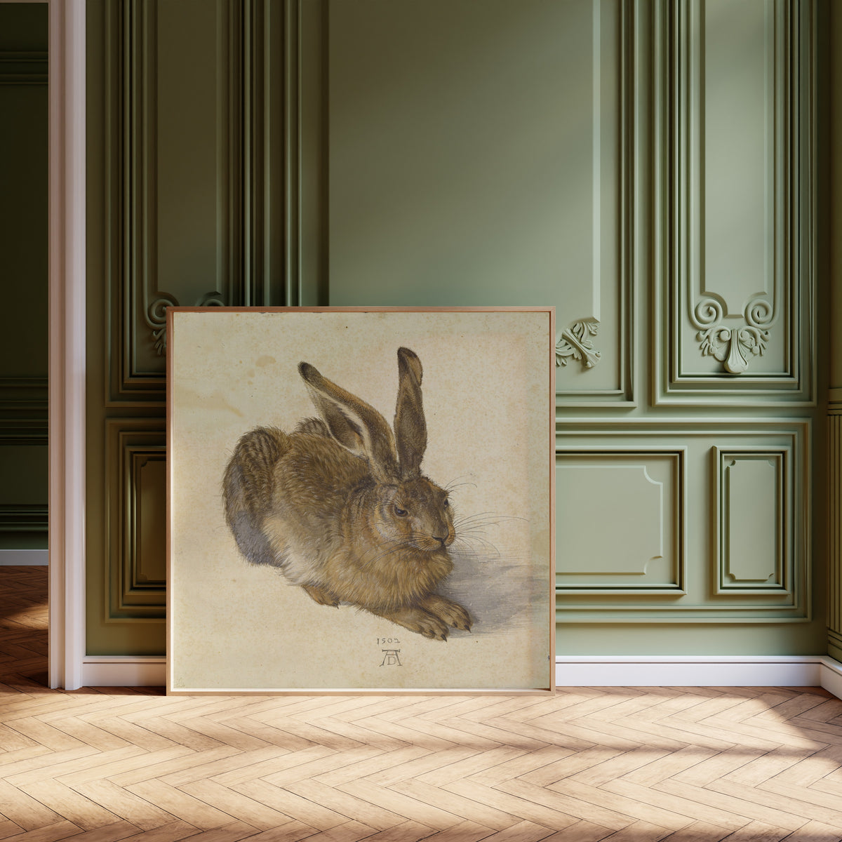 Framed art print of Young Hare by Albrecht Dürer, leaning against olive-green panelling on a herringbone floor