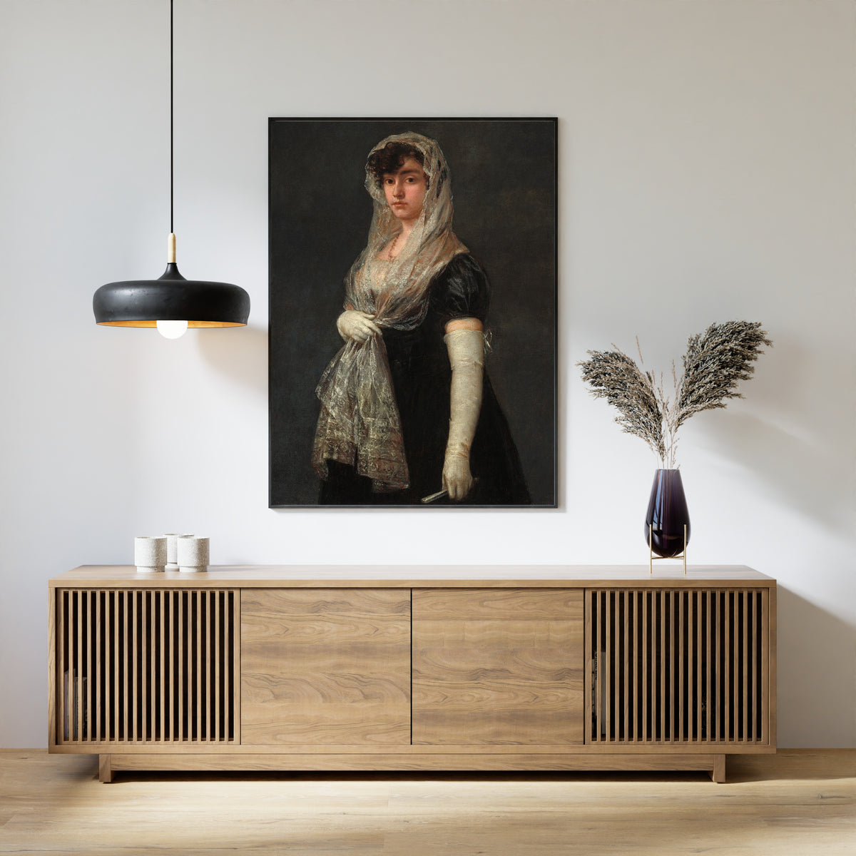 Framed art print of Young Lady Wearing a Mantilla and Basquina by Francisco de Goya, above a slatted wood sideboard