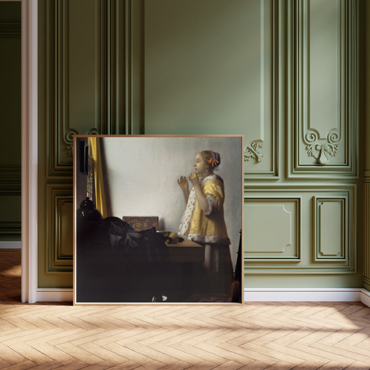 Framed art print of Young Woman with a Pearl Necklace by Johannes Vermeer, leaning against olive-green panelling on a herringbone floor