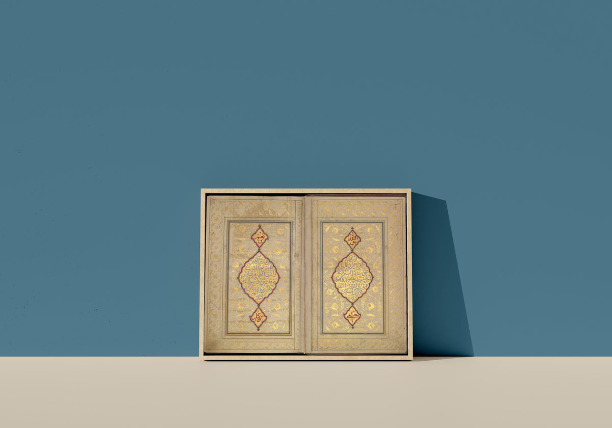 Framed art print of Book of Prayers: Illuminated Opening with Gold Medallions by Ahmad Nairizi, in a light wood frame leaning on a blue wall