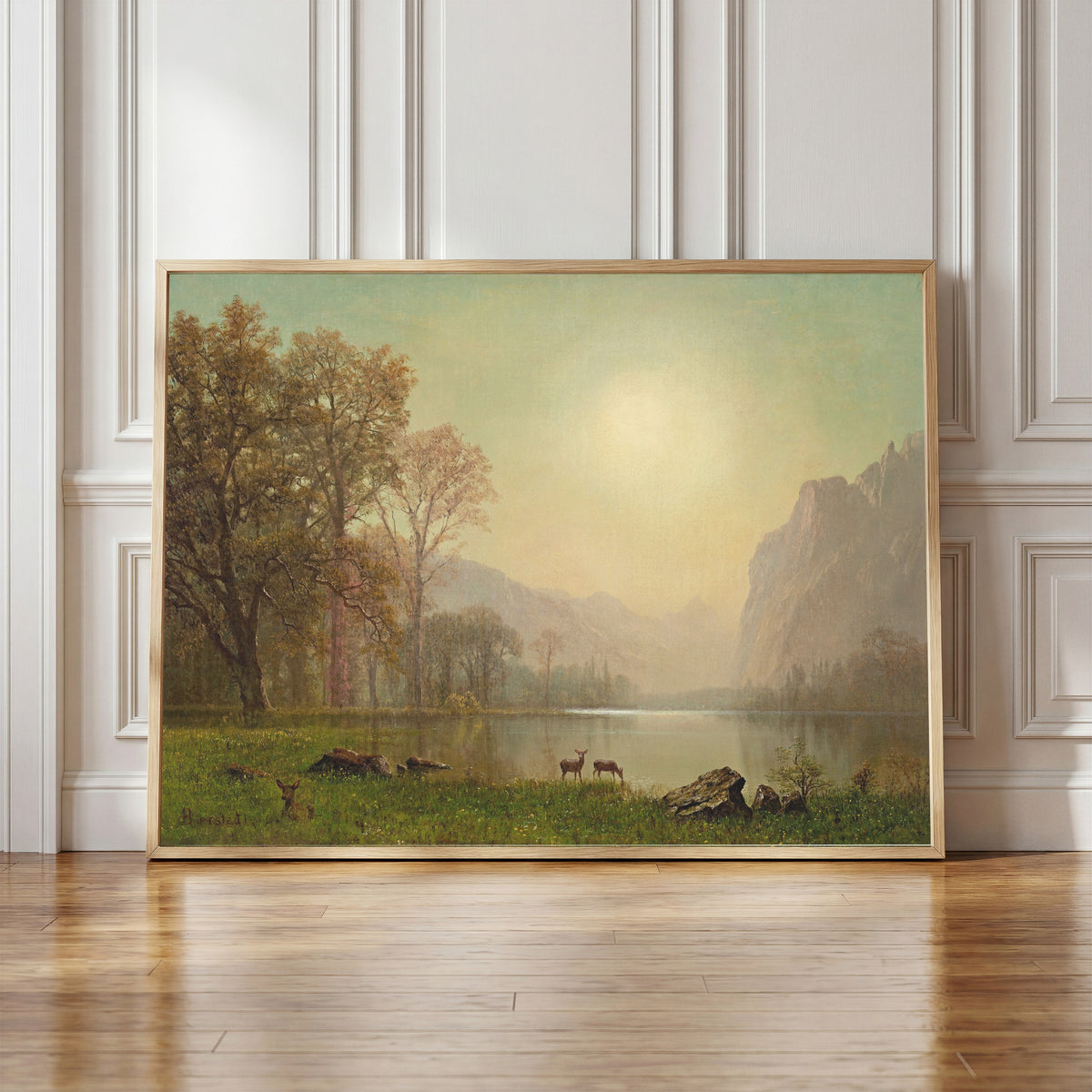 Framed art print of Dawn in the Rockies by Albert Bierstadt, in a light wood frame leaning against a panelled white wall