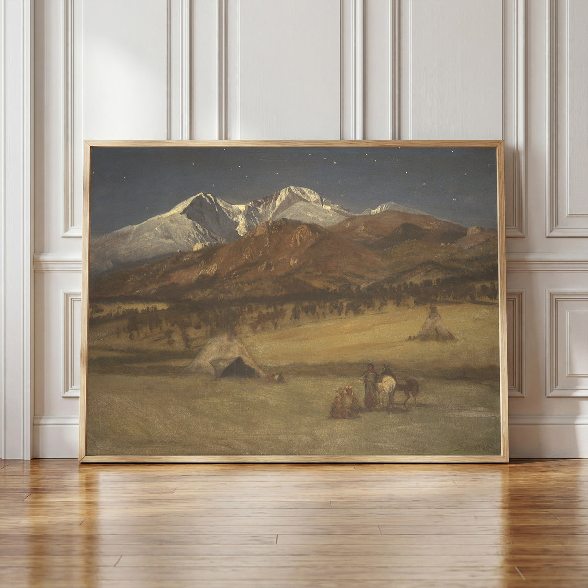 Framed art print of Indian Encampment – Evening by Albert Bierstadt, in a light wood frame leaning against a panelled white wall