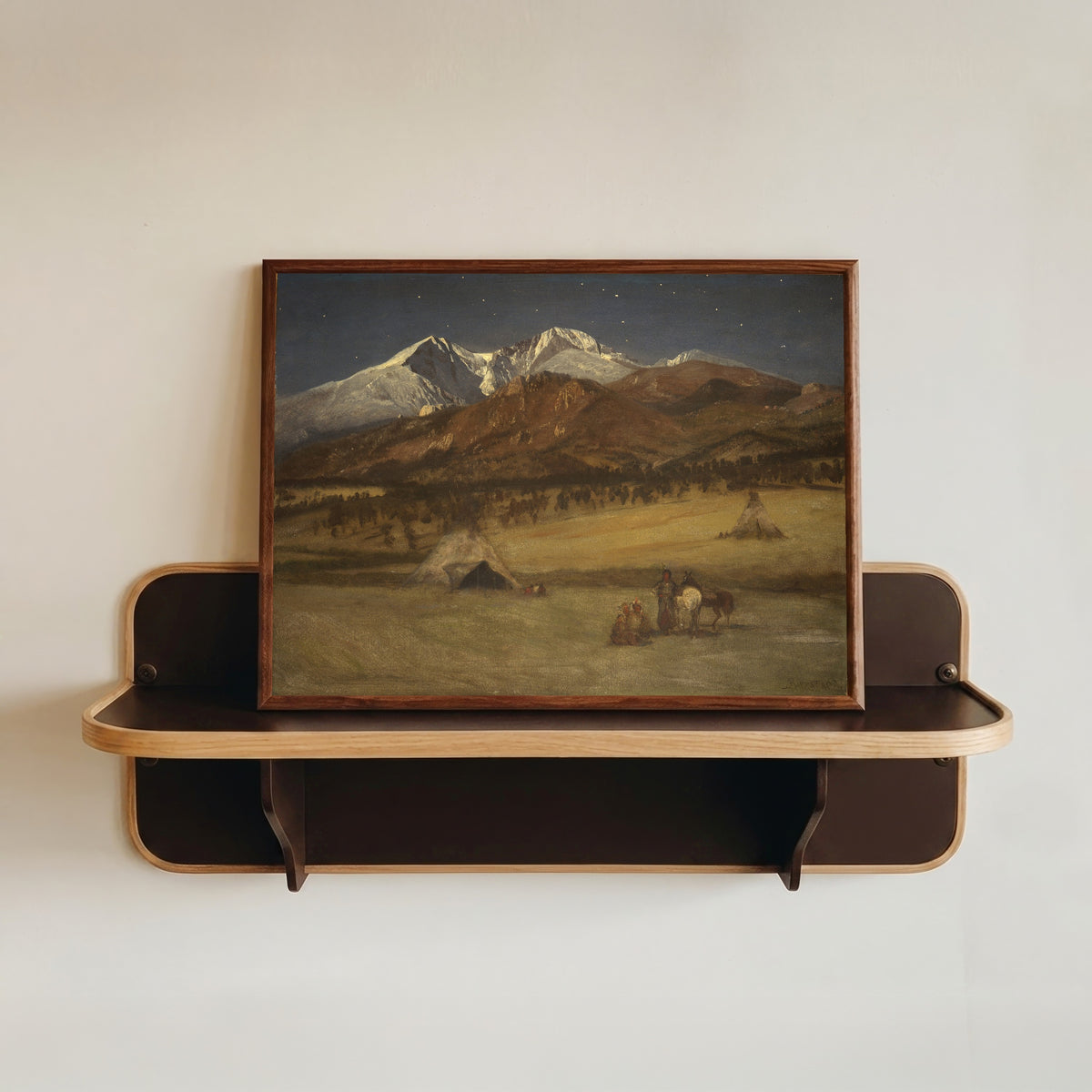 Framed art print of Indian Encampment – Evening by Albert Bierstadt, in a dark wood frame resting on a wall shelf