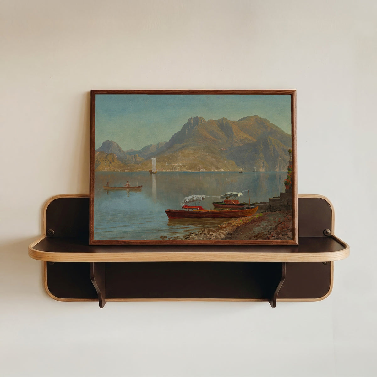 Framed art print of Lake Como by Albert Bierstadt, in a dark wood frame resting on a wall shelf
