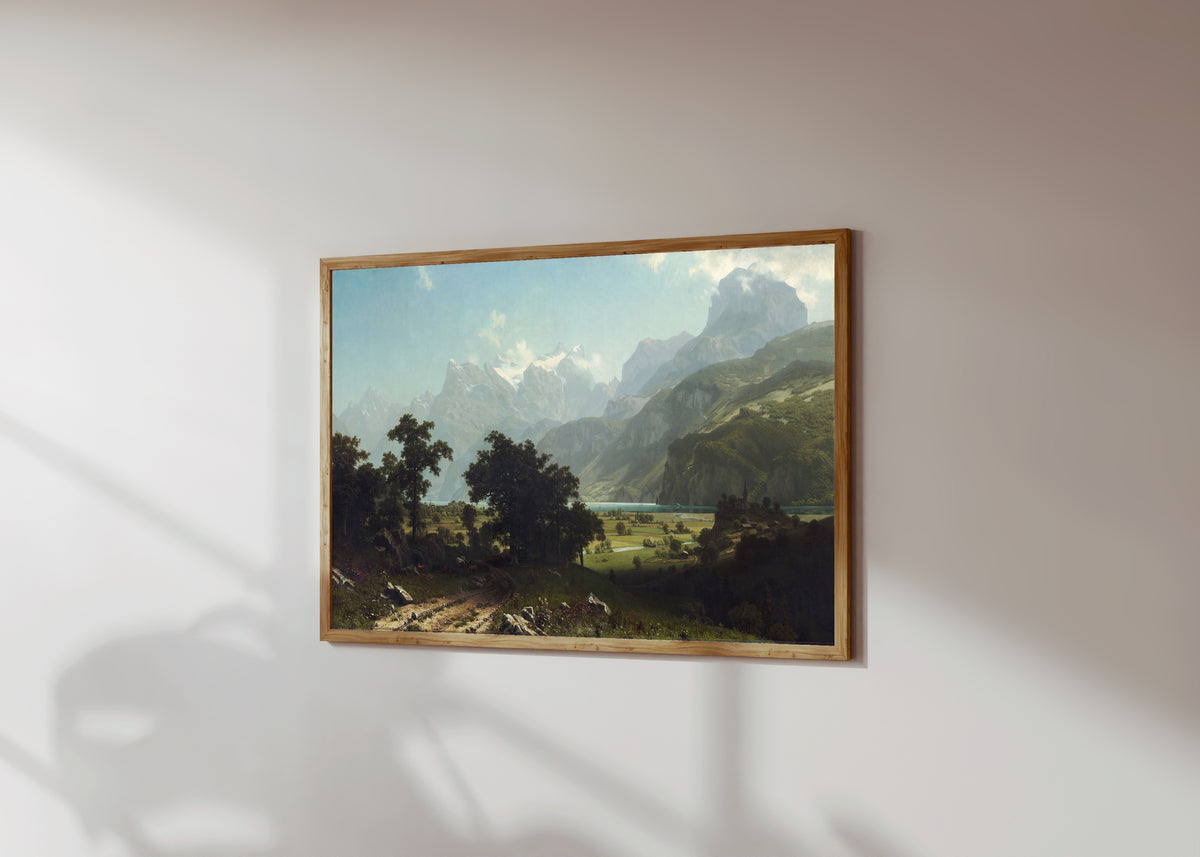 Framed art print of Lake Lucerne by Albert Bierstadt, in a light wood frame on a sunlit white wall, seen at a slight angle