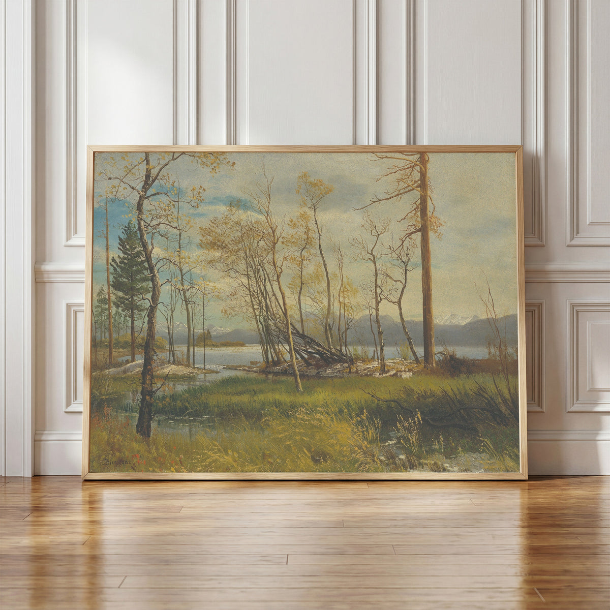 Framed art print of Lake Tahoe by Albert Bierstadt, in a light wood frame leaning against a panelled white wall