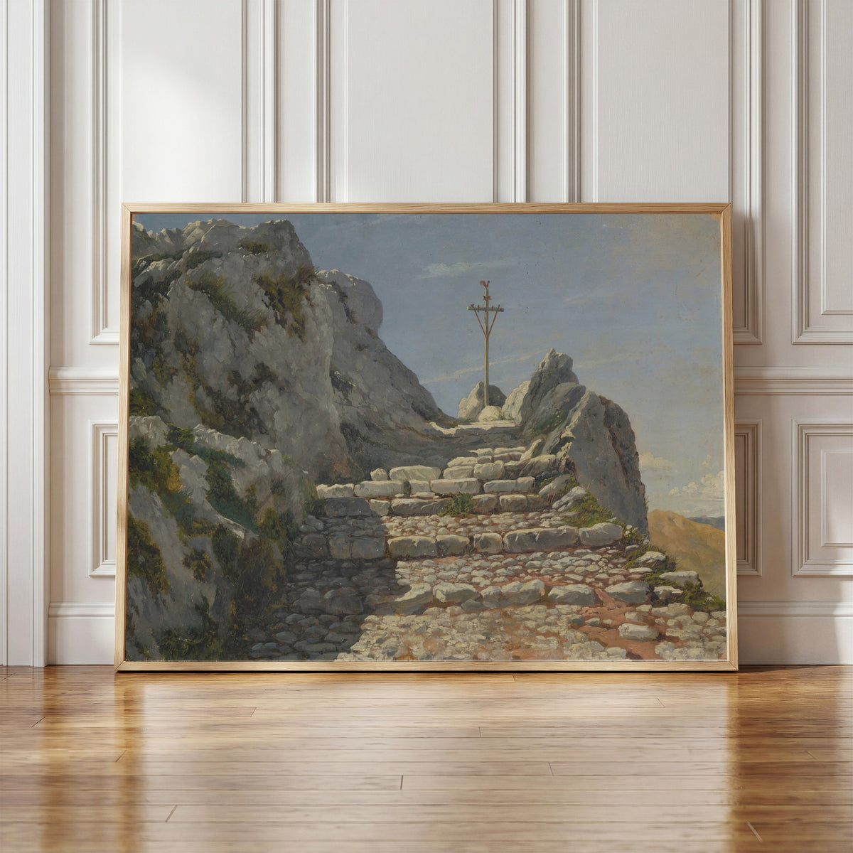 Framed art print of Landscape by Albert Bierstadt, in a light wood frame leaning against a panelled white wall