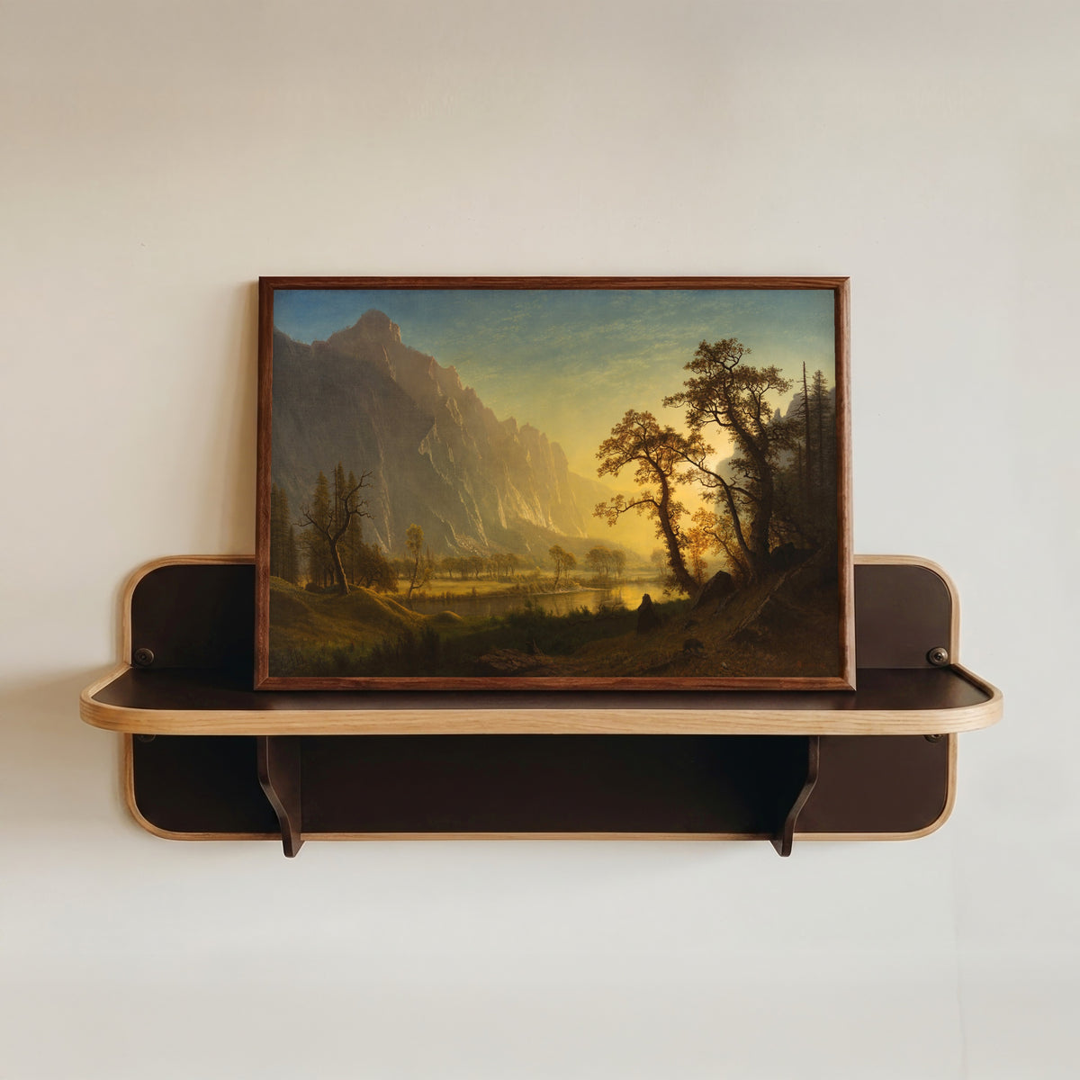 Framed art print of Sunrise, Yosemite Valley by Albert Bierstadt, in a dark wood frame resting on a wall shelf