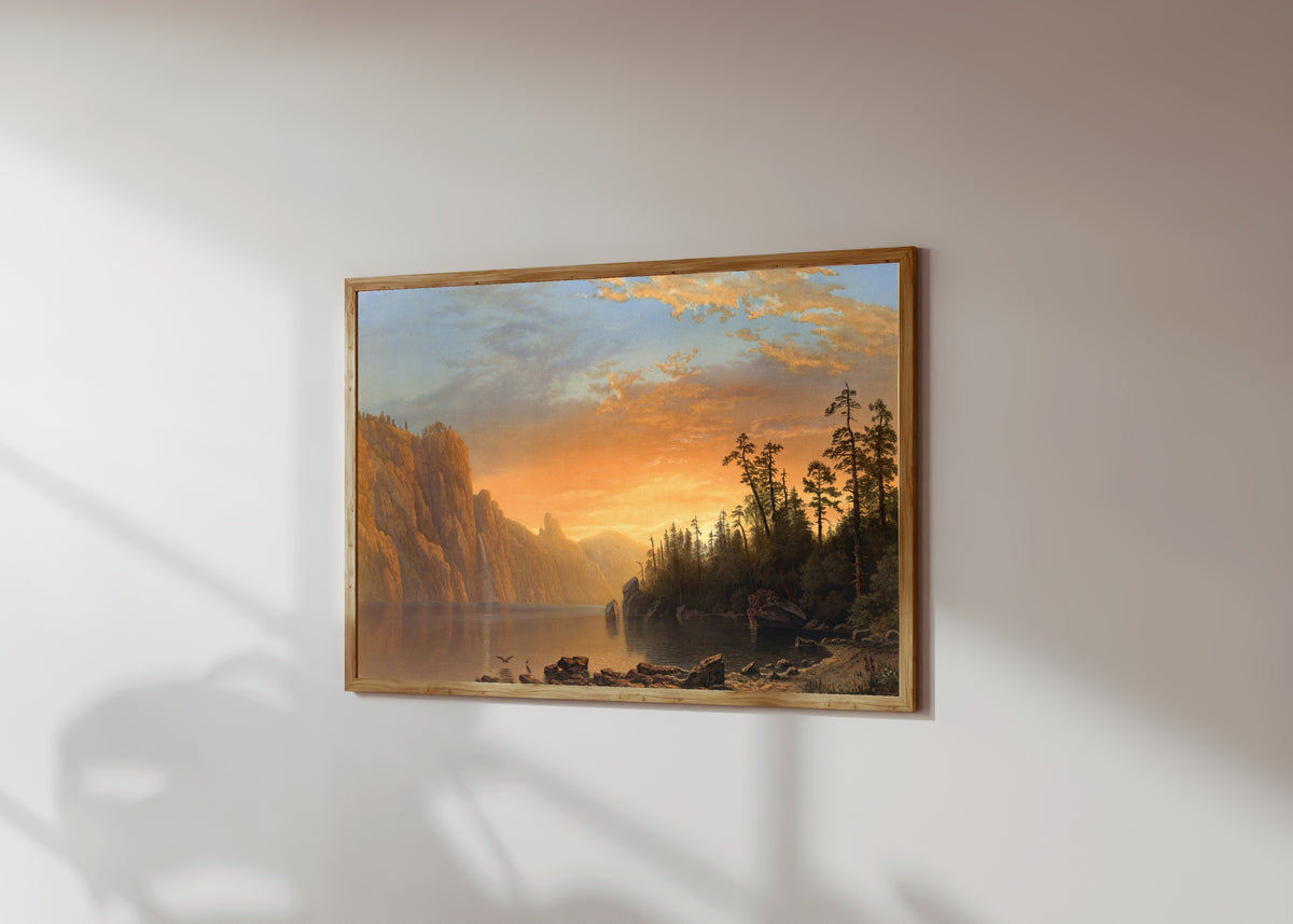 Framed art print of Sunset in California by Albert Bierstadt, in a light wood frame on a sunlit white wall, seen at a slight angle
