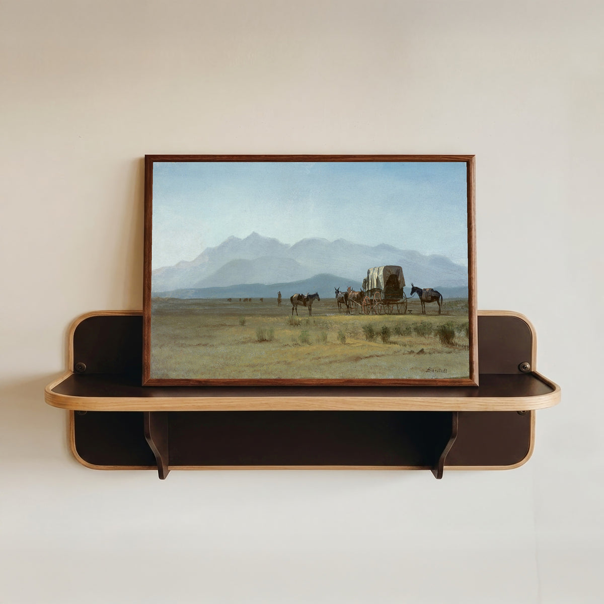 Framed art print of Surveyor's Wagon in the Rockies by Albert Bierstadt, in a dark wood frame resting on a wall shelf