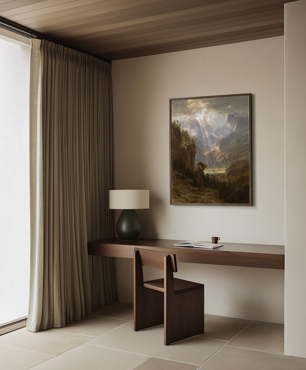 Framed art print of The Rocky Mountains, Lander's Peak (Alternate Version) by Albert Bierstadt, in a dark wood frame on a plaster wall above a walnut desk