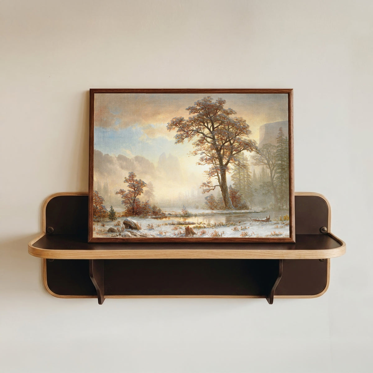 Framed art print of First Snowfall of the Year by Albert Bierstadt, in a dark wood frame resting on a wall shelf