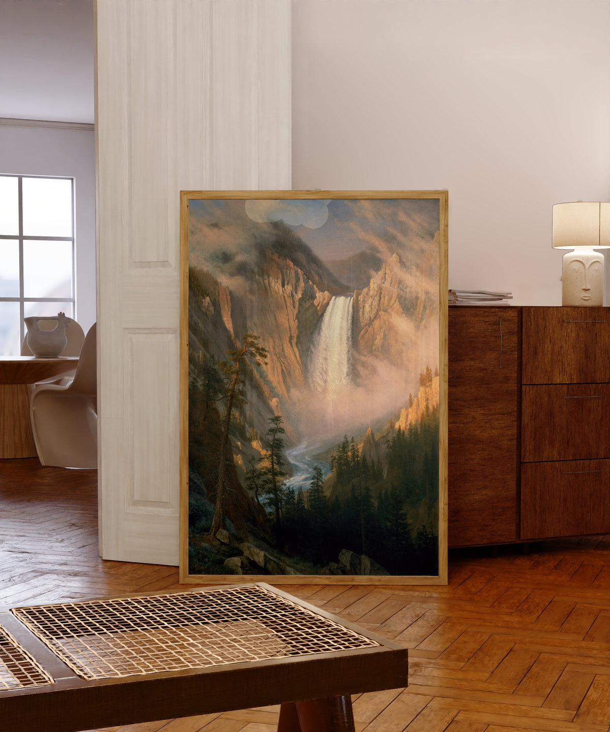 Framed art print of Yellowstone Falls by Albert Bierstadt, in a light wood frame leaning in a warm room with a parquet floor