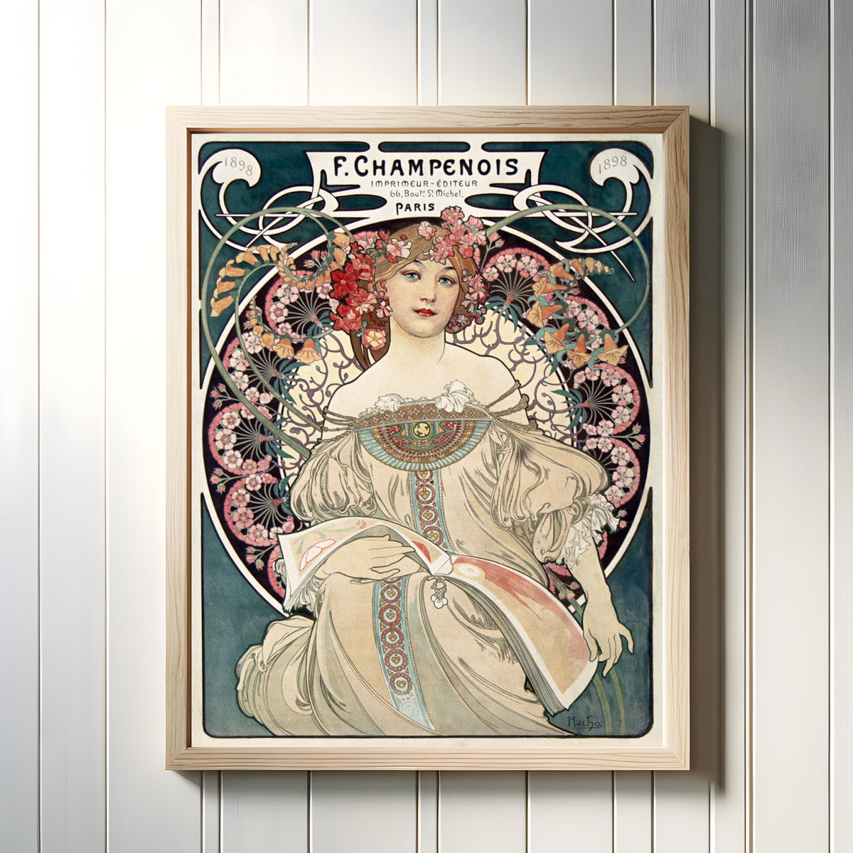 Framed art print of F. Champenois Imprimeur-Éditeur by Alphonse Mucha, in a light wood frame on a white panelled wall