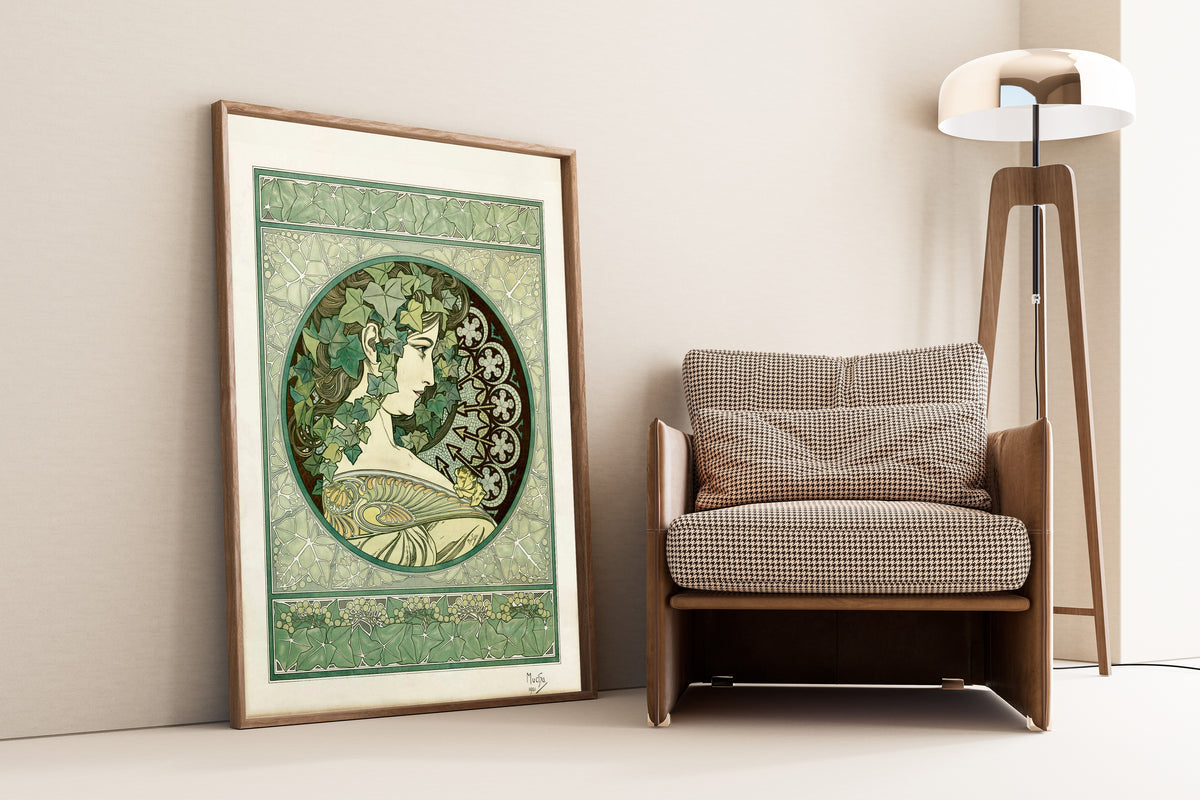 Framed art print of Ivy by Alphonse Mucha, leaning against a wall beside an armchair and a floor lamp
