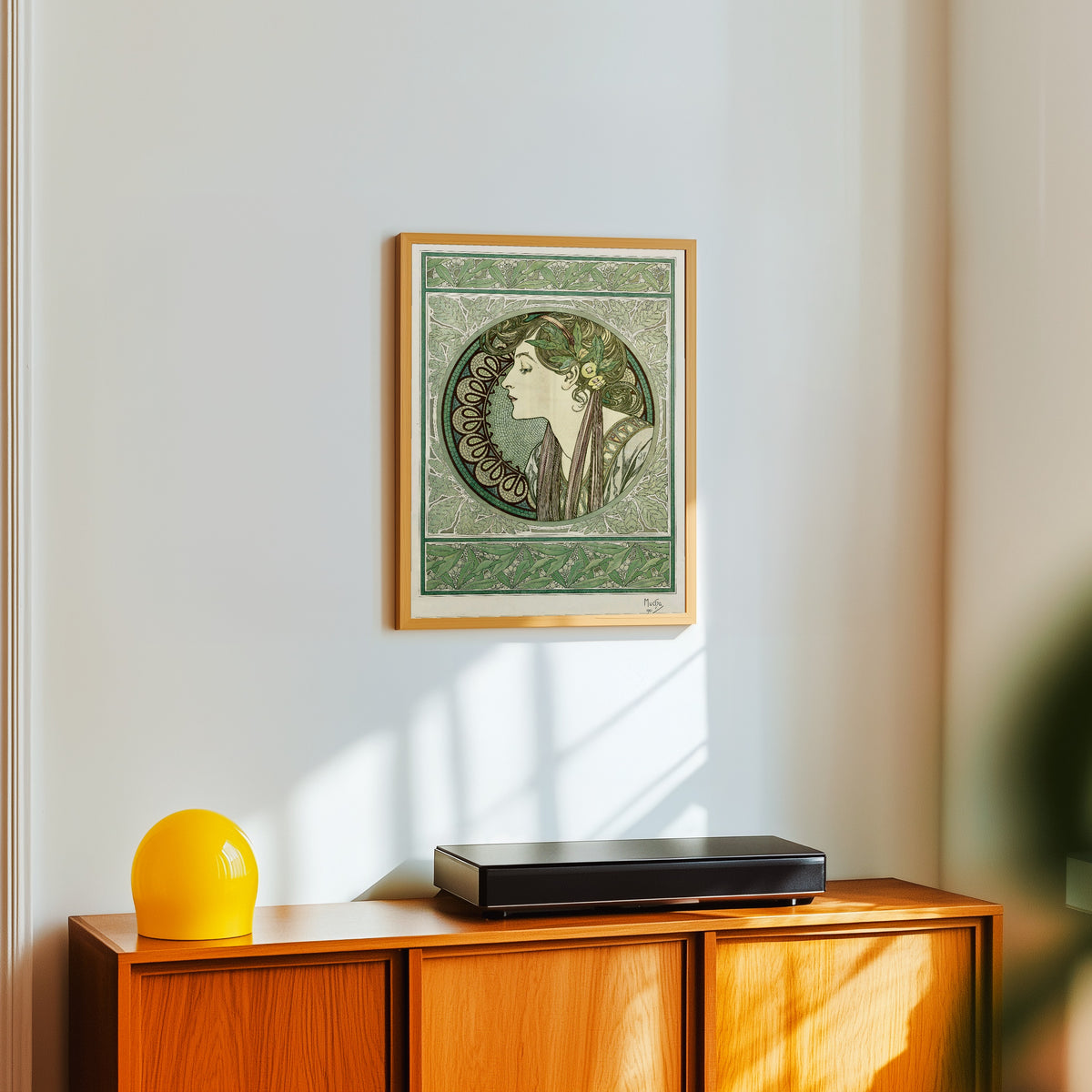 Framed art print of Laurel by Alphonse Mucha, in a light wood frame on a white wall above an orange sideboard