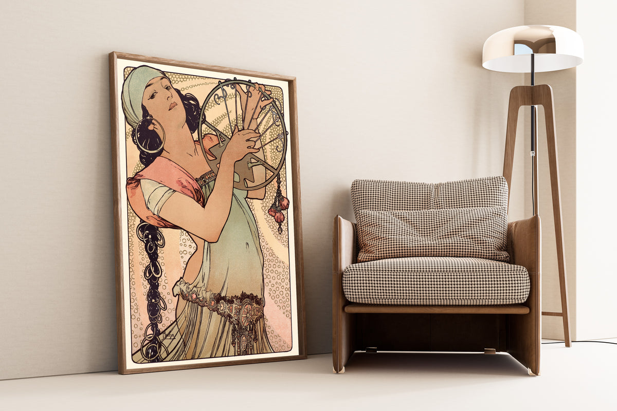 Framed art print of Salomé by Alphonse Mucha, leaning against a wall beside an armchair and a floor lamp
