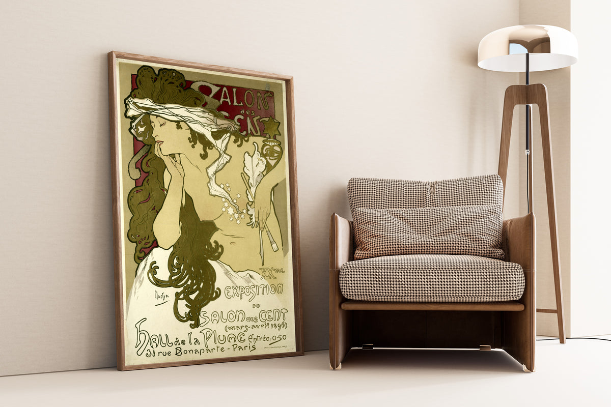Framed art print of Salon des Cent, XXe Exposition (mars-avril 1896) by Alphonse Mucha, leaning against a wall beside an armchair and a floor lamp