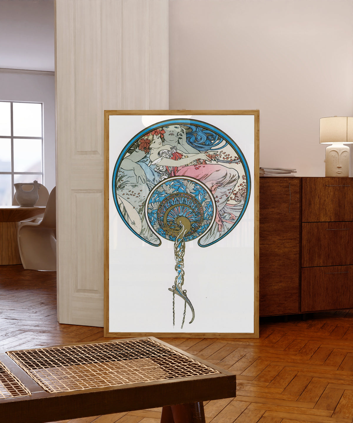 Framed art print of The Passing Wind Takes Youth Away by Alphonse Mucha, in a light wood frame leaning in a warm room with a parquet floor