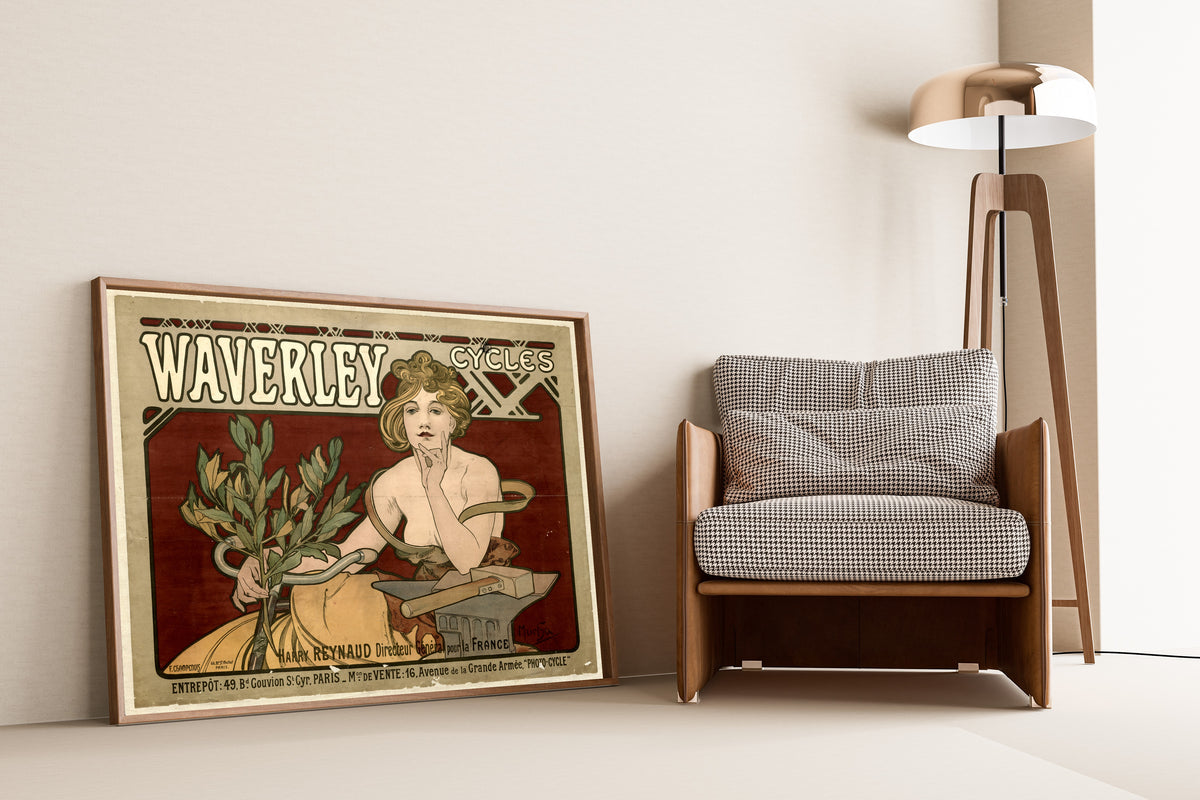 Framed art print of Waverley Cycles by Alphonse Mucha, leaning against a wall beside an armchair and a floor lamp