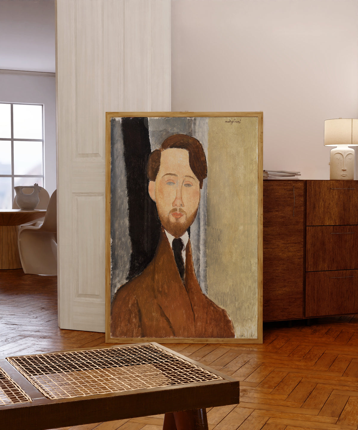 Framed art print of Léopold Zborowski by Amedeo Modigliani, in a light wood frame leaning in a warm room with a parquet floor