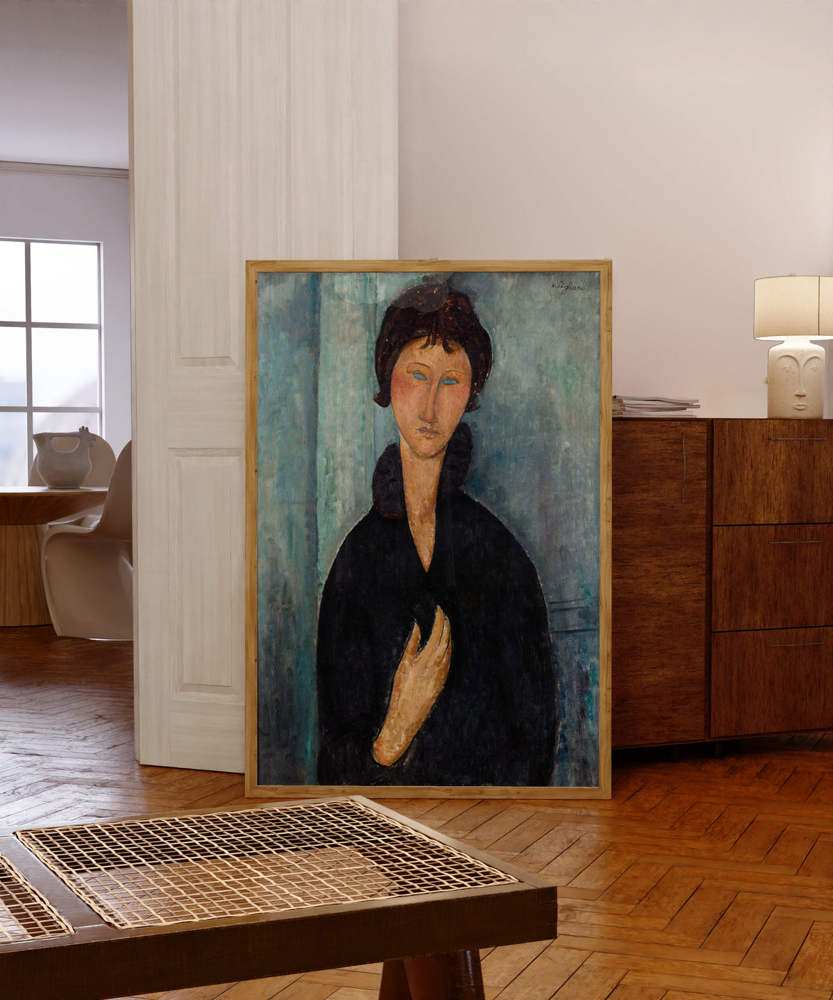 Framed art print of Woman with Blue Eyes by Amedeo Modigliani, in a light wood frame leaning in a warm room with a parquet floor