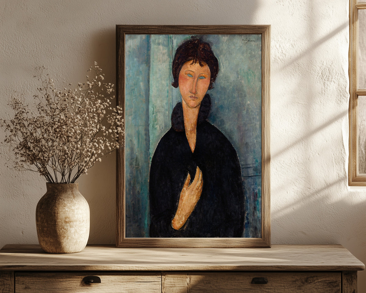 Framed art print of Woman with Blue Eyes by Amedeo Modigliani, in a dark wood frame leaning on a rustic console beside dried flowers