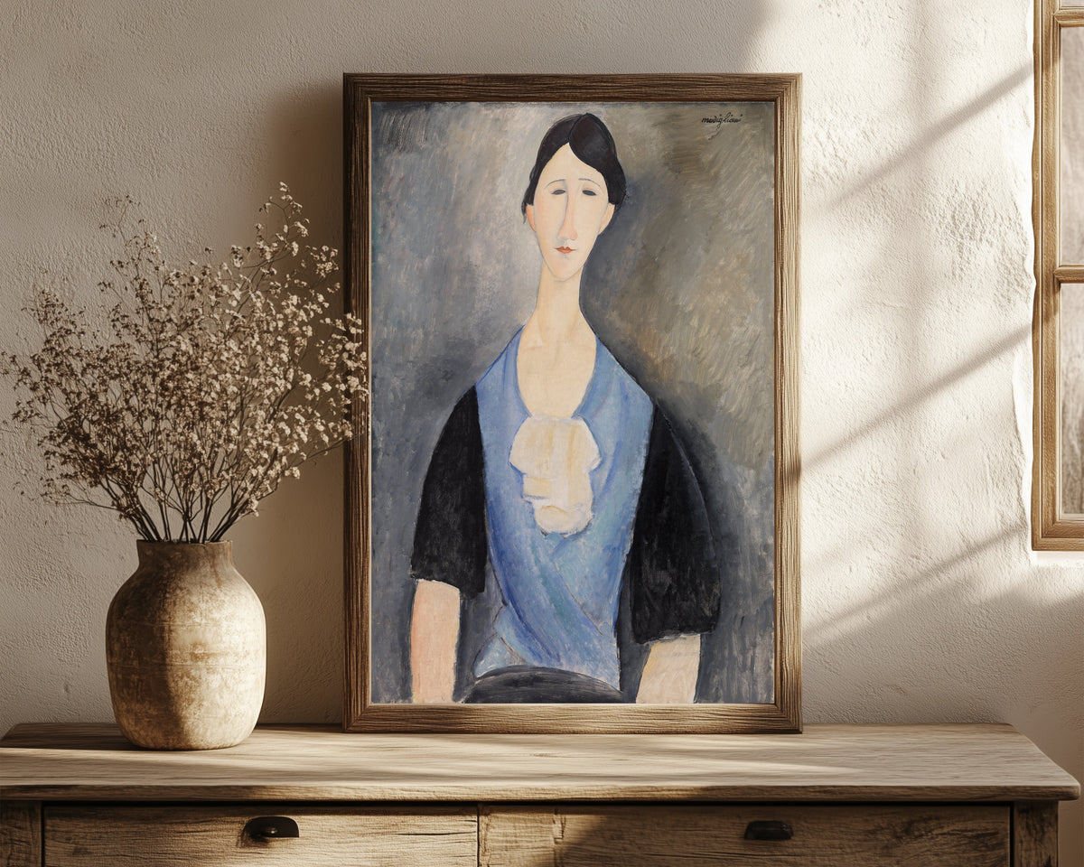 Framed art print of Young Woman in Blue by Amedeo Modigliani, in a dark wood frame leaning on a rustic console beside dried flowers