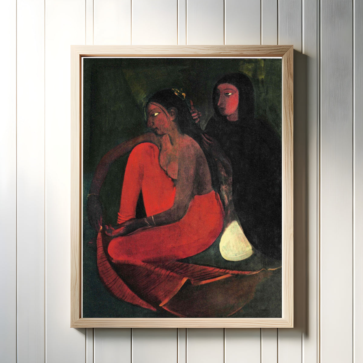 Framed art print of Dressing the Bride (1937) by Amrita Sher-Gil, in a light wood frame on a white panelled wall