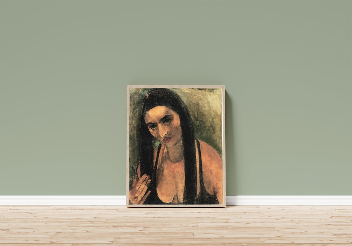 Framed art print of Self-Portrait with Long Hair (1934) by Amrita Sher-Gil, in a light wood frame leaning on a sage green wall above a wooden floor
