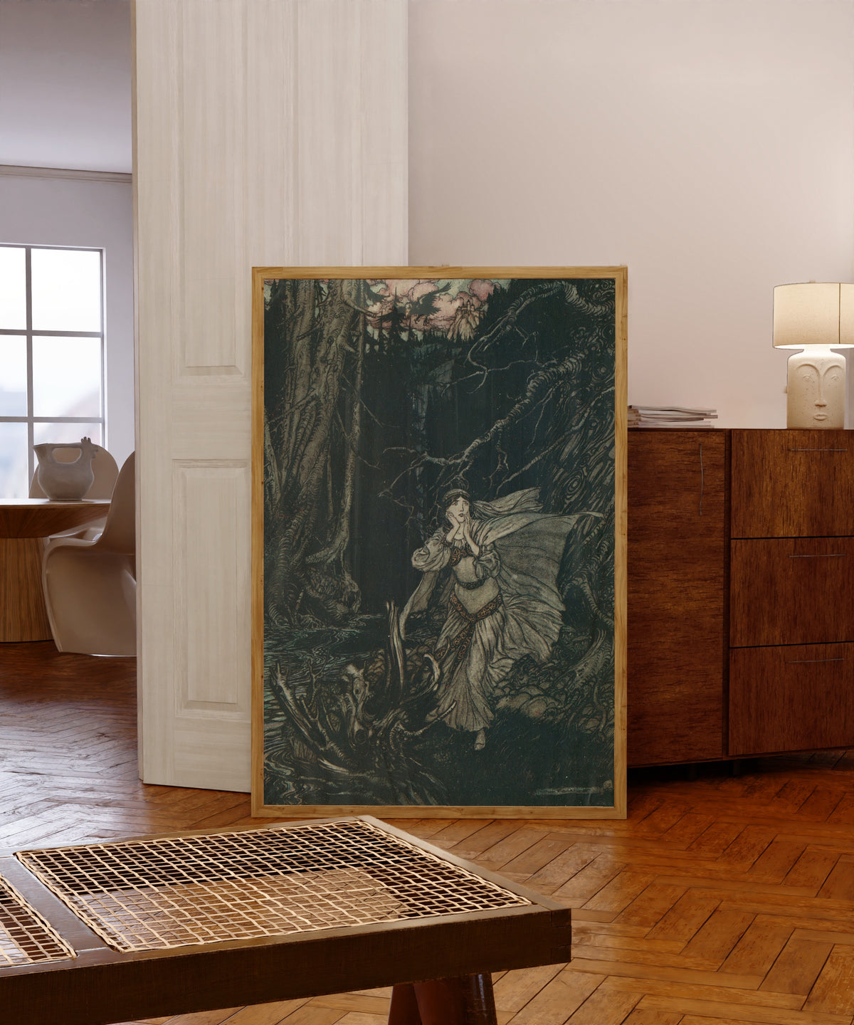 Framed art print of Bertalda in the Black Valley by Arthur Rackham, in a light wood frame leaning in a warm room with a parquet floor
