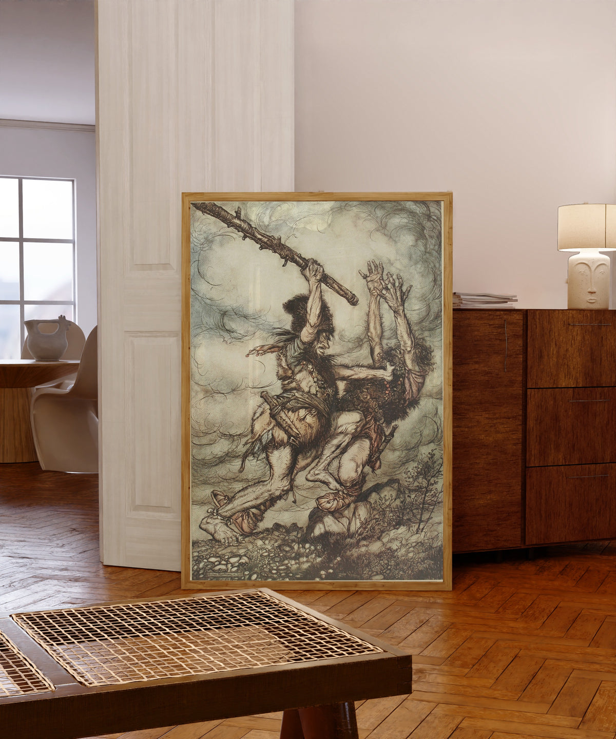 Framed art print of Fafner Kills Fasolt by Arthur Rackham, in a light wood frame leaning in a warm room with a parquet floor