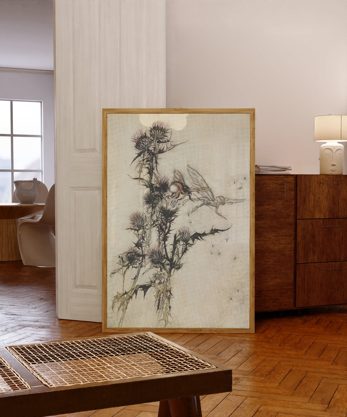 Framed art print of Kill Me a Red-Hipped Humble-Bee on the Top of a Thistle by Arthur Rackham, in a light wood frame leaning in a warm room with a parquet floor