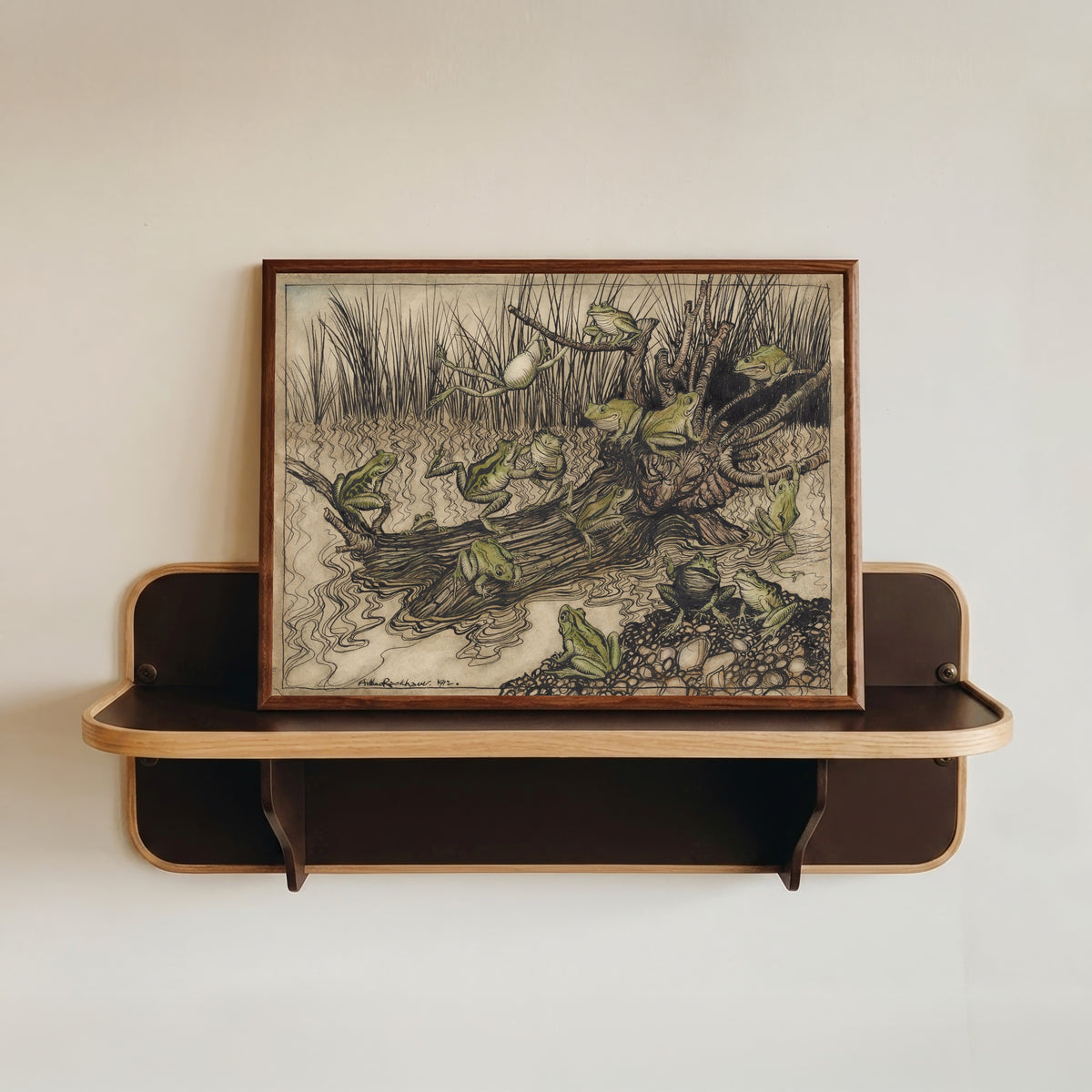 Framed art print of King Log by Arthur Rackham, in a dark wood frame resting on a wall shelf