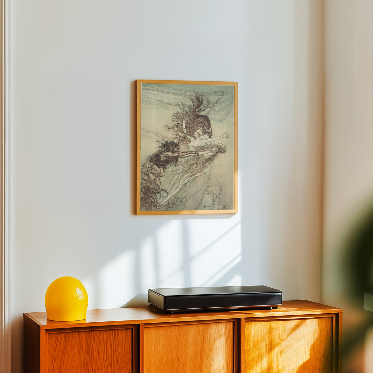 Framed art print of The Rhine-Maidens Teasing Alberich by Arthur Rackham, in a light wood frame on a white wall above an orange sideboard